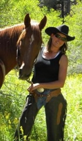 Woman in western chaps standing with a Chesnutt horse.